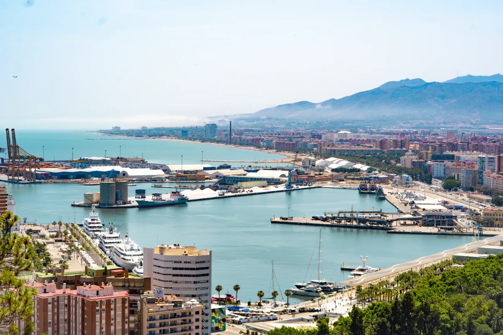 Vista de Málaga com porto, prédios à beira-mar e céu azul ensolarado
