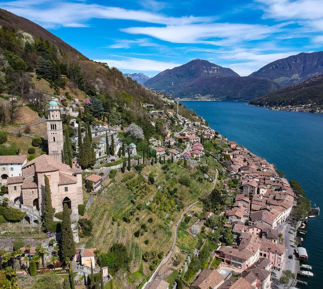 Vista de Morcote à beira do lago, com casario em encosta e colinas ao fundo.