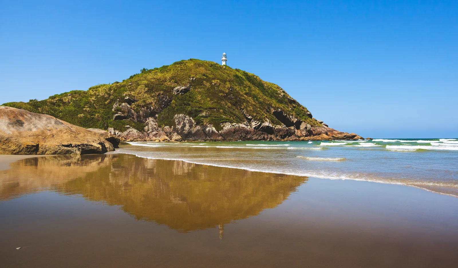 Beach on Ilha do Mel with blue sea and a strip of sand surrounded by vegetation.