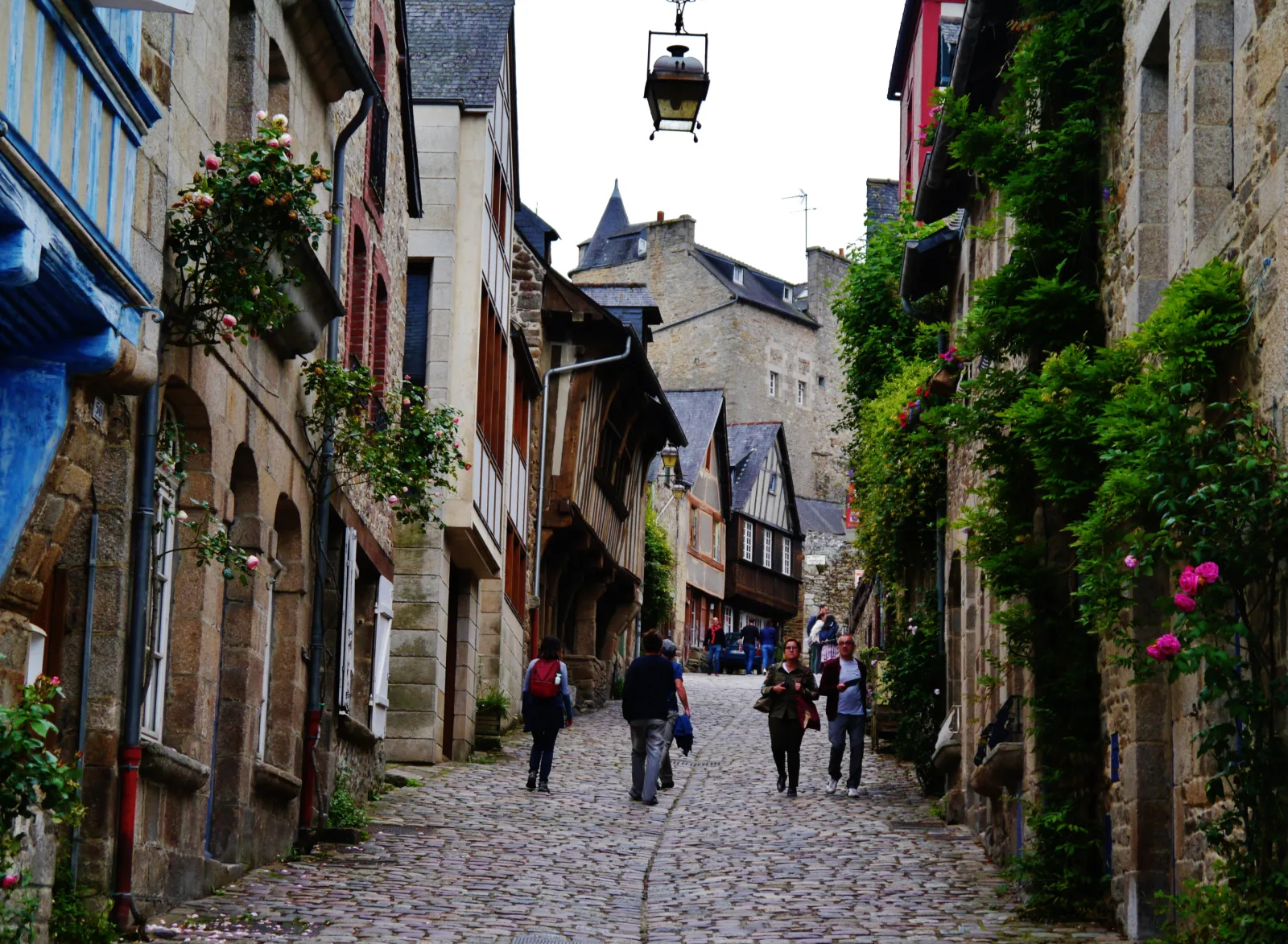 Rua de pedra íngreme em Dinan, com casas históricas e caminho descendente até o porto
