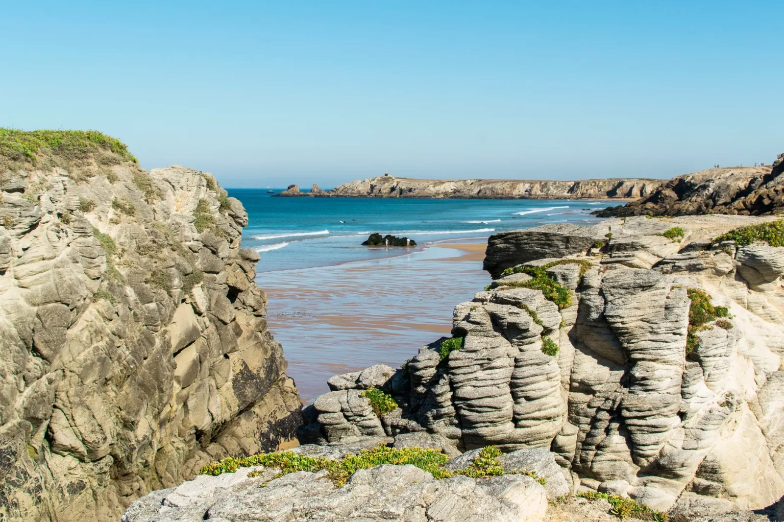 Playa ventosa en Quiberon con mar agitado, ideal para surf y windsurf, rodeada de acantilados.