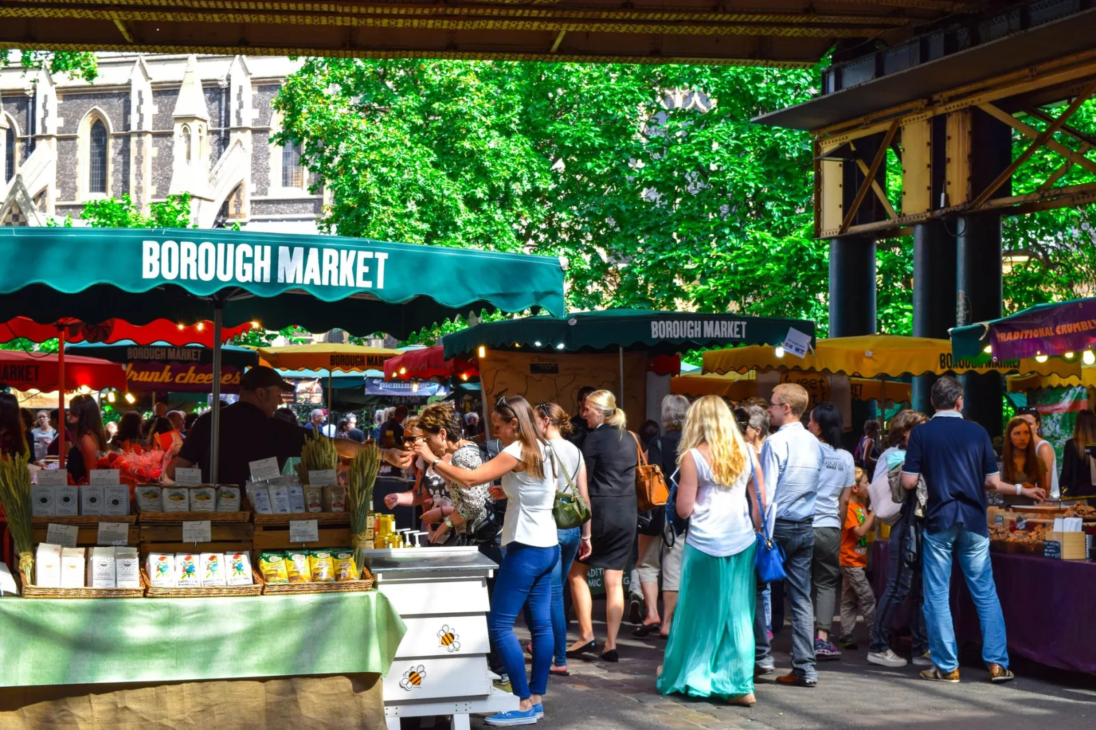 Food stalls and shops in a lively market in London, with people walking around.