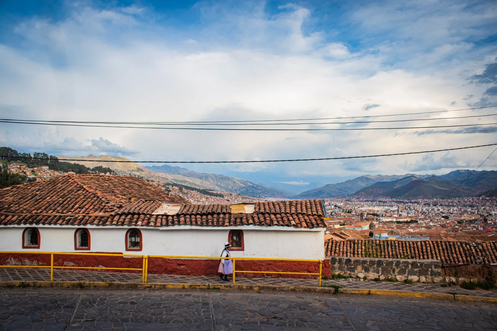 Calle inclinada de Cusco con peatones caminando y coches subiendo la vía alta del centro histórico