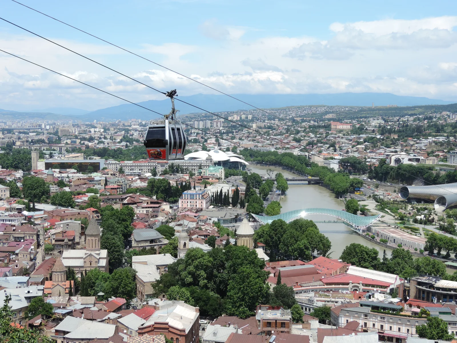 Teleférico en Tiflis subiendo hacia la colina, con vista de la ciudad al fondo.