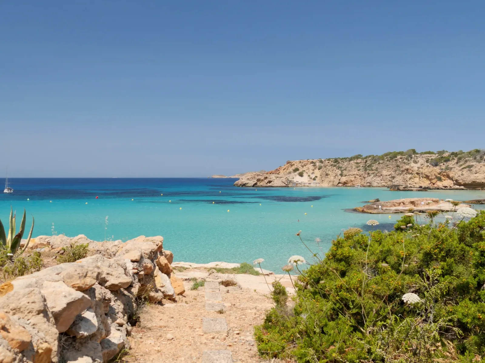 Ibiza beach with turquoise blue sea, light sand, and cliffs in the background.