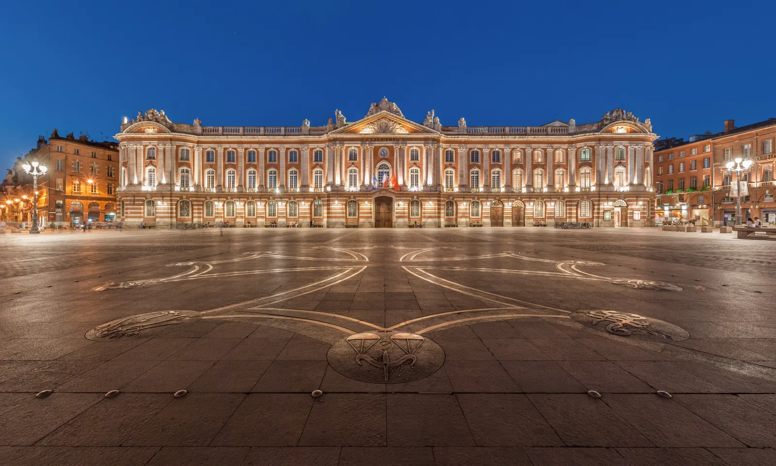 Vista de la Place du Capitole en Toulouse, con fachadas rosadas y movimiento en la plaza