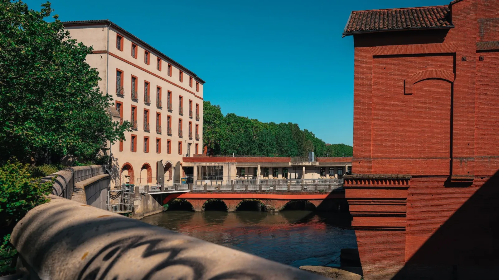 Pareja y familias pasean por una plaza histórica de Toulouse, entre edificios rosados y cafés al aire libre