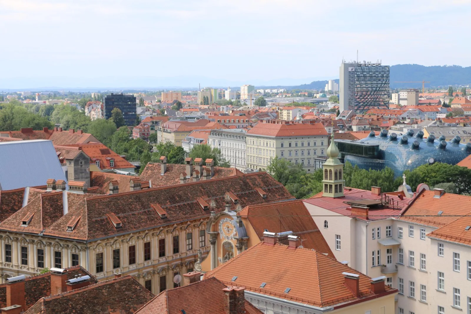 Vista panorâmica de Graz ao entardecer, com telhados históricos e o rio refletindo a cidade.