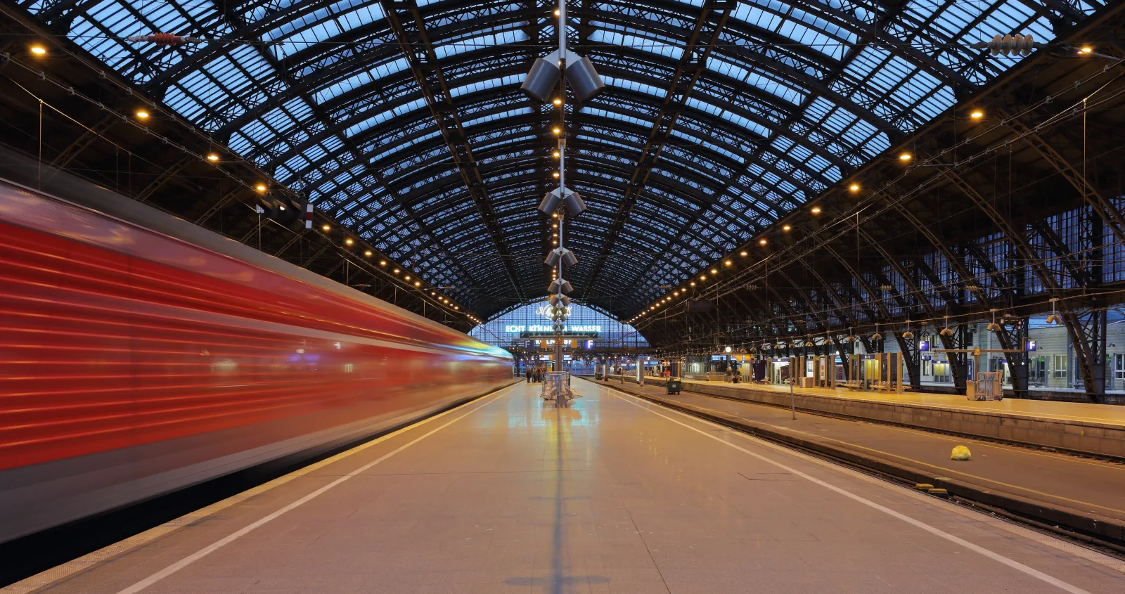 Entrance of Köln HBF station with Cologne Cathedral in the background and tourists arriving.