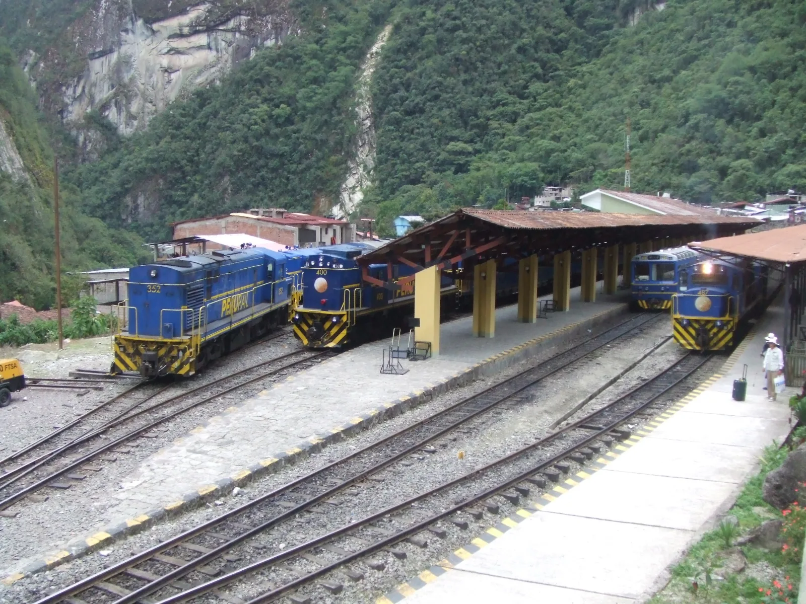 Tourist train arriving in Aguas Calientes, on the route via Ollantaytambo, amid lush green mountains.