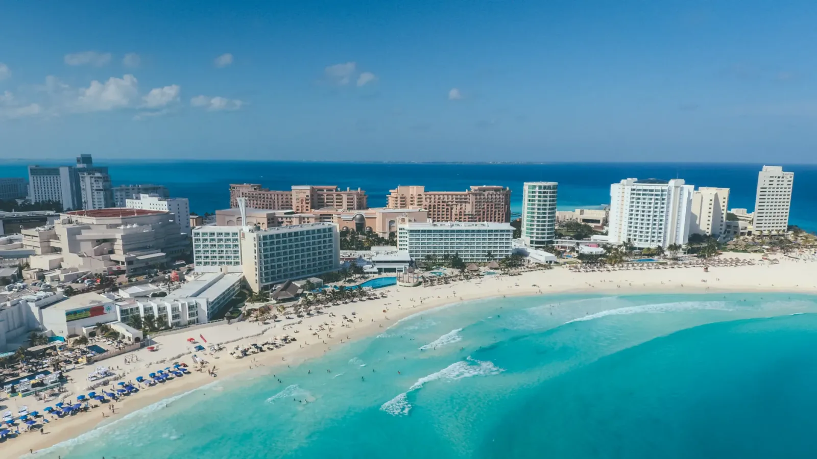 Playa de Cancún con mar azul turquesa y cocoteros bajo cielo soleado