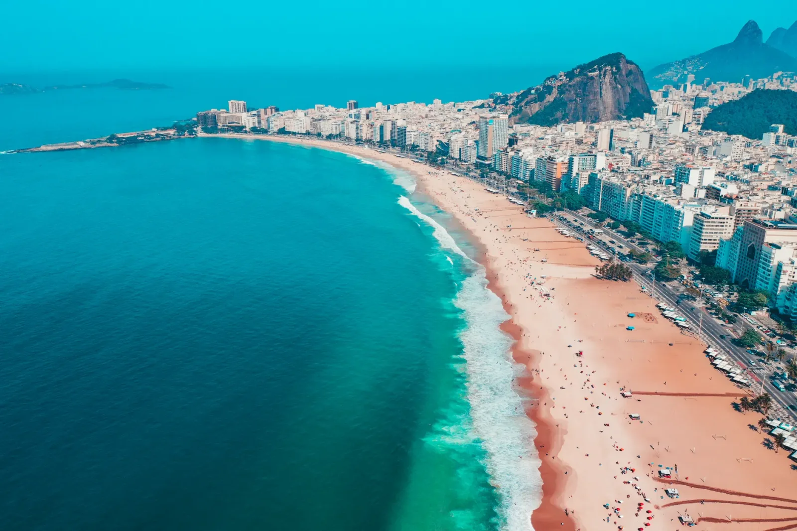 Praia do Rio de Janeiro sob sol forte e céu parcialmente nublado, com clima típico de verão.