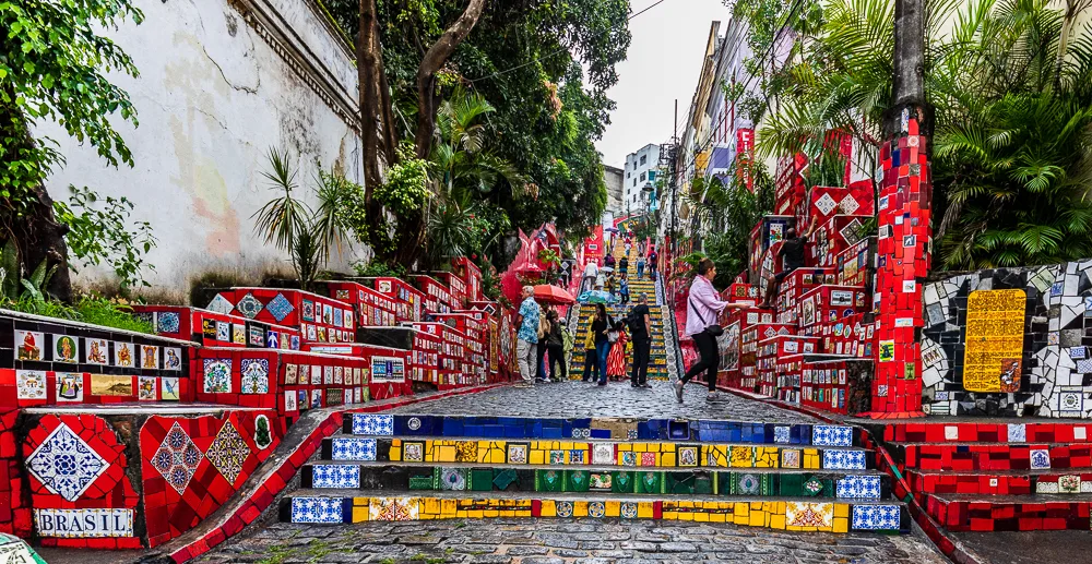 Escadaria Selarón colorida no Rio de Janeiro, com turistas subindo os degraus.