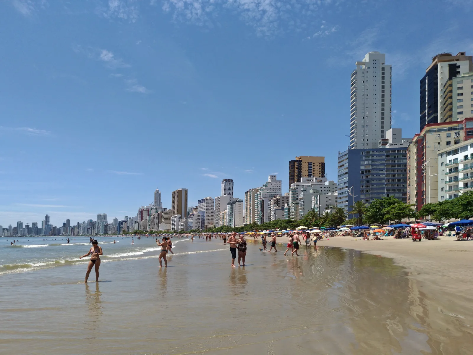 Praia de Balneário Camboriú com mar azul, faixa de areia e mata costeira ao fundo
