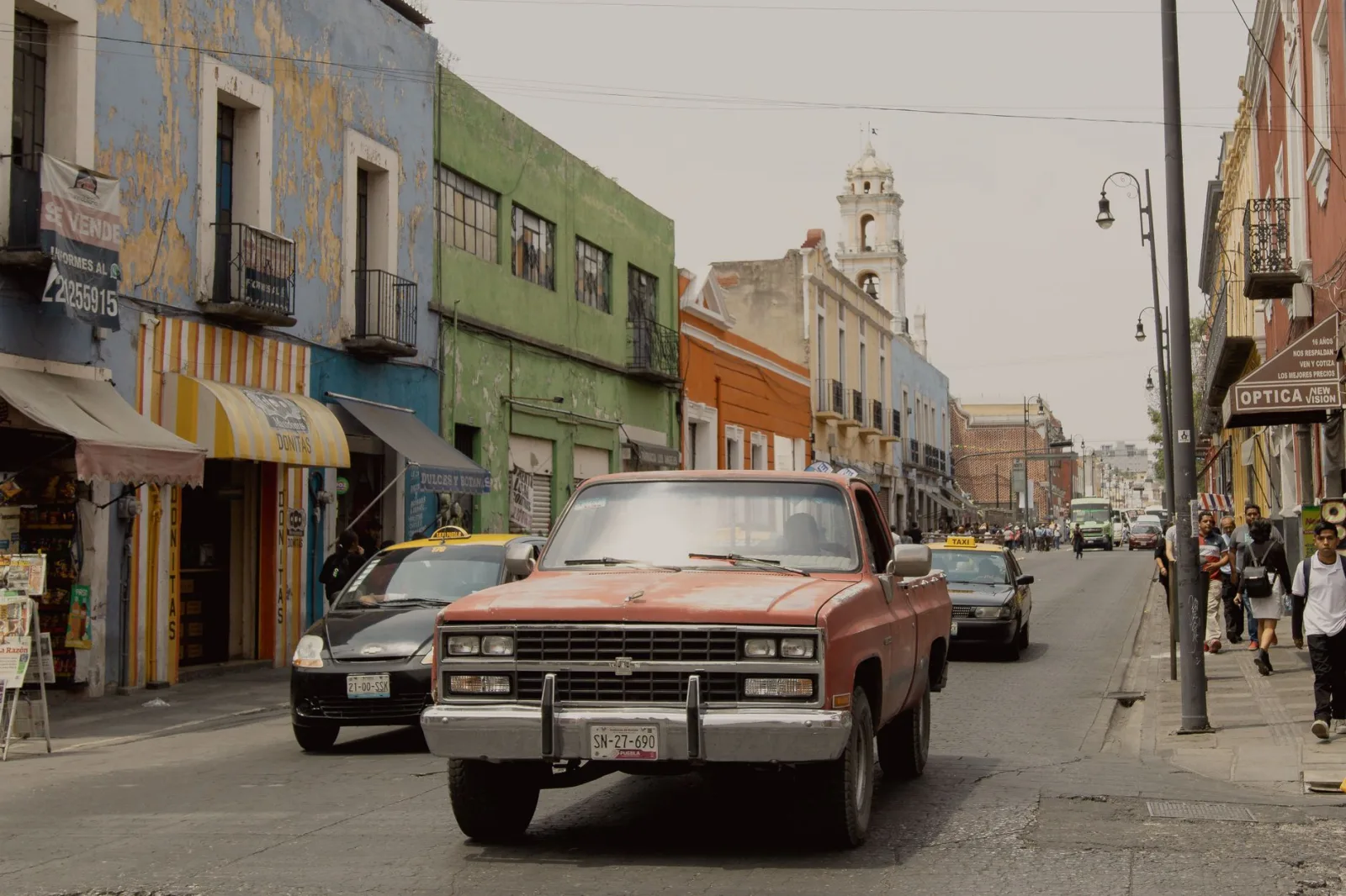 Calle histórica de Puebla con peatones y tráfico ligero, sugiriendo movilidad a pie y en taxi.