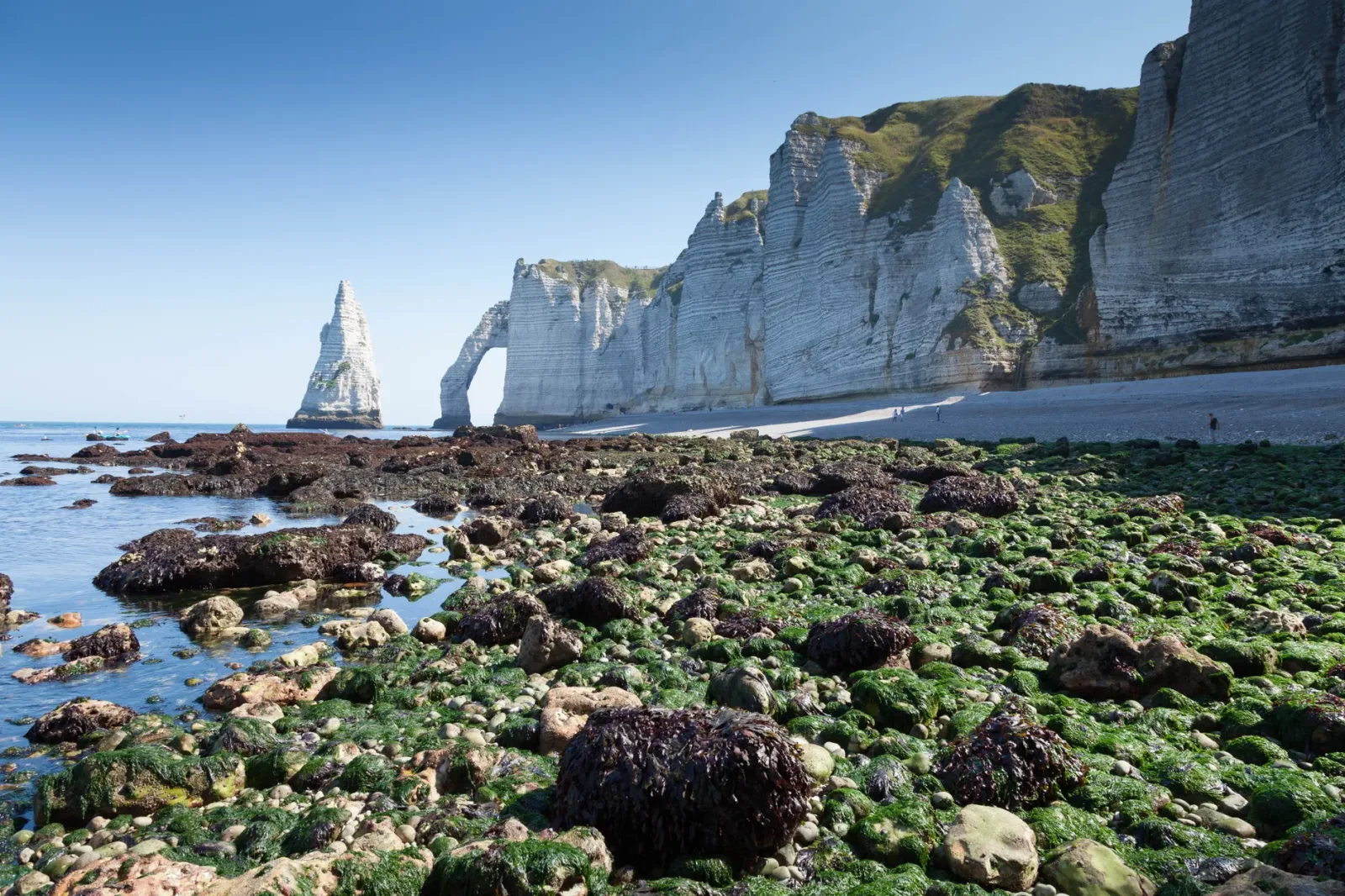 Praia de cascalhos em Étretat com pessoas na Promenade Perrey, ouvindo as ondas e a maré.