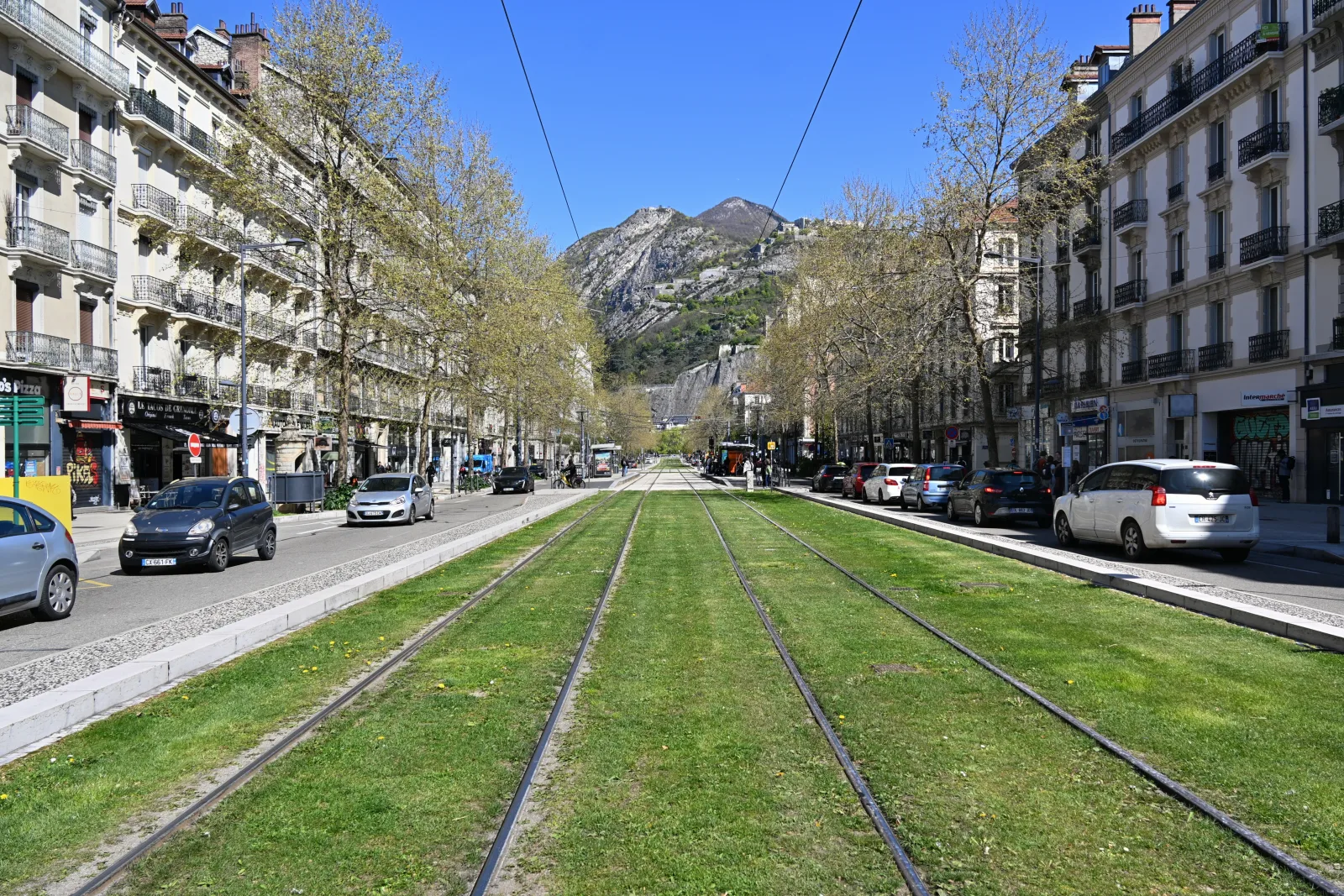 Vista panorâmica de Grenoble entre montanhas, com o rio ao fundo e clima urbano alpino.