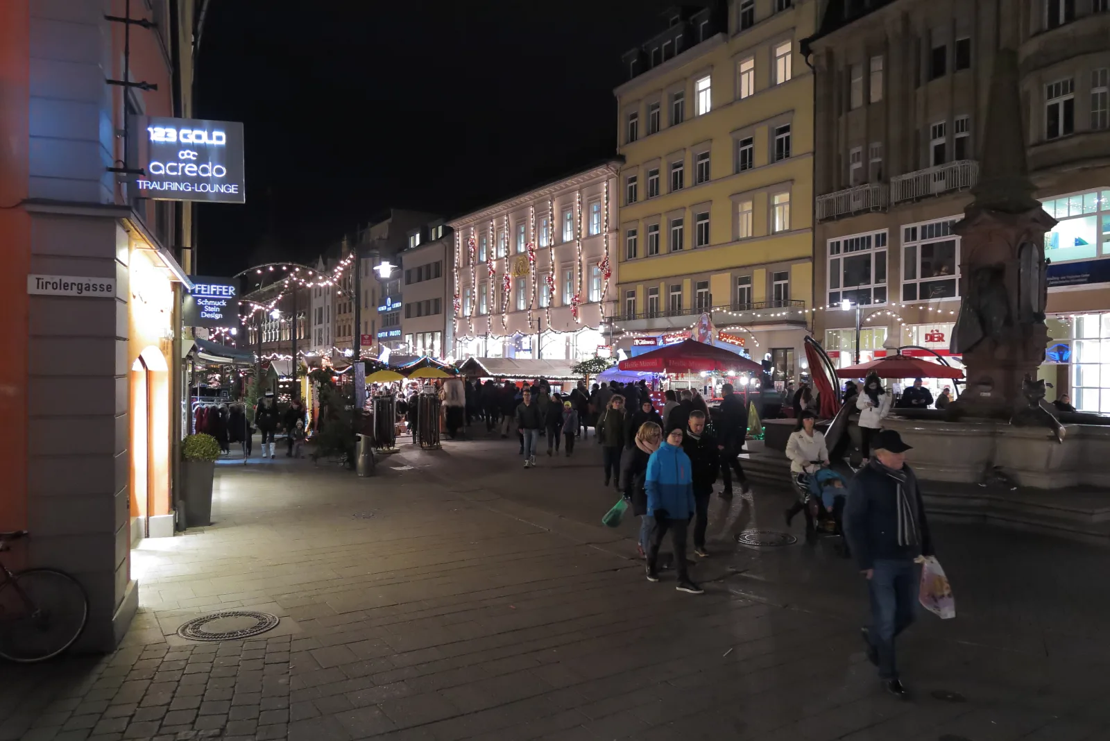 Stands iluminados do Mercado de Natal de Konstanz, com visitantes e Glühwein à beira do lago.